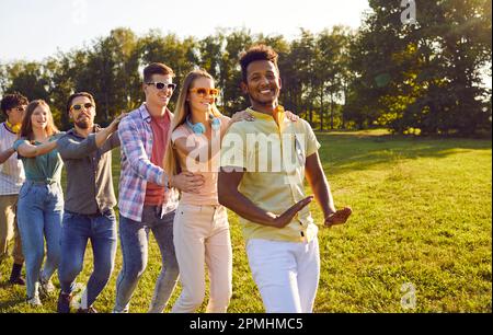 Gente allegra che gioca i treni simulati che tengono le spalle l'un l'altro durante il divertimento nel parco estivo. Foto Stock