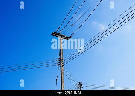 Una vista panoramica dei poli telefonici e dei cavi elettrici sopra un bel cielo blu Foto Stock
