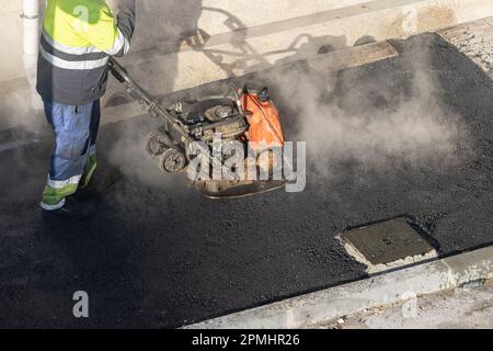 Lavoratore con una macchina compattatrice a piastre vibranti che lavora su una strada cittadina Foto Stock