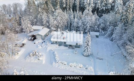 Vista aerea intorno ad un uomo che rimuove la neve da un tetto di casa con pannelli solari, in una giornata di sole inverno Foto Stock