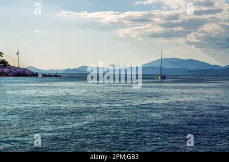 Tramonto su Hydra una delle isole greche e grande barca a vela che si avvicina al porto e giorno. In lontananza colline di Mainland della Grecia Foto Stock