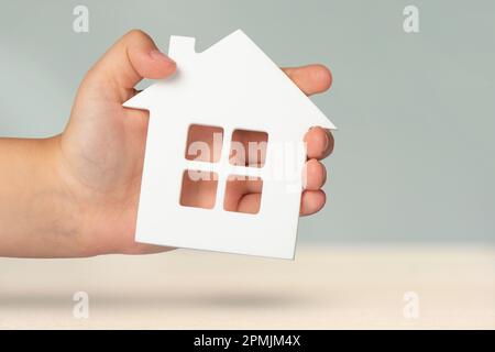 Assicurazione immobiliare. Modello di una casa bianca in mani su uno sfondo grigio sfocato. Assicurare una casa o un appartamento, il concetto di servizi assicurativi Foto Stock