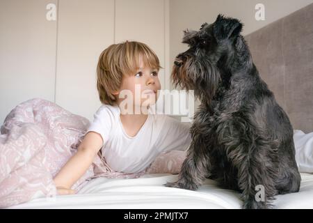 Carino bambino biondo, ragazzo toddler, sdraiato sul letto con il suo cane da compagnia a casa Foto Stock