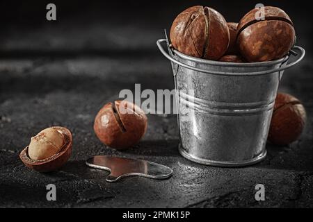 Noci di Macadamia spaccate in piccolo secchio su sfondo ardesia Foto Stock