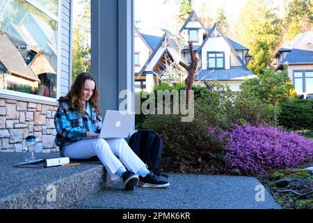 La ragazza apre la valigetta preparandosi a fare i compiti l'adolescente si siede sul portico in jeans bianchi occhiali blu giacca sulla testa crema solare bottiglia d'acqua in zaino venire dalla scuola a riposo clima caldo Canada Foto Stock