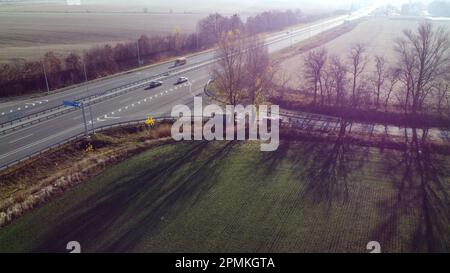 Bella strada panoramica, auto, campi agricoli dopo il raccolto il giorno di sole autunno. Vista dall'alto della strada automobilistica con diverse auto che guidano. Luce solare, luce abbagliante. Vista aerea del drone Foto Stock