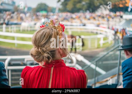 Donna in vestito rosso indossando bella fasminator guardare i cavalli sfilare prima della gara Foto Stock