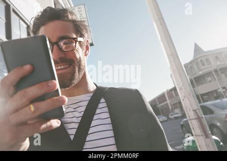 Connesso in ogni fase del percorso. un giovane uomo alla moda che usa un cellulare mentre cammina in città. Foto Stock