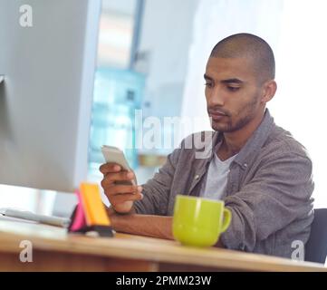 Ricezione di nuove istruzioni di progettazione. un progettista che utilizza un cellulare mentre lavora su un computer in un ufficio. Foto Stock