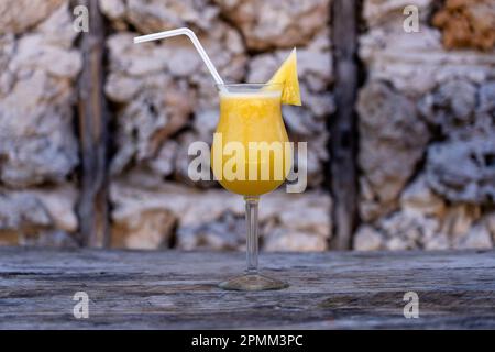 Spremuta di fresco di ananas in un calice di vetro sullo sfondo di un vecchio muro di pietra. Isola di Zanzibar, Tanzania, Africa orientale. Primo piano, c Foto Stock