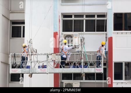 Ascensore per ponteggi con 3 pittori che dipingono un nuovo strato di vernice bianca sull'esterno dell'alloggiamento per dare una facciata esterna fresca. Singapore. Foto Stock