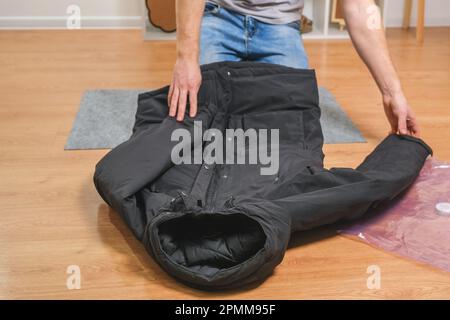 Un uomo piega giacche invernali e li mette in un sacchetto sottovuoto per conservare la stagione nell'armadio. Risparmio di spazio e conservazione accurata dei vestiti. Organizzazione Foto Stock