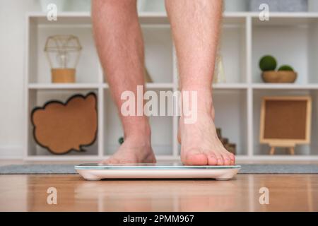 Un uomo si trova sulla bilancia. Il ragazzo sta pesando se stesso. Bilance da pavimento per la salute. Controllo del peso. Foto Stock