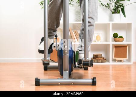 Un uomo si allena su una macchina ellittica. Allenatore sportivo a casa in appartamento. Sport a casa. Foto Stock