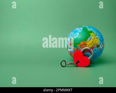 Serratura rossa a forma di cuore con chiave e globo terrestre su sfondo verde. Concetto di amore natura per sempre con lucchetto. Foto Stock