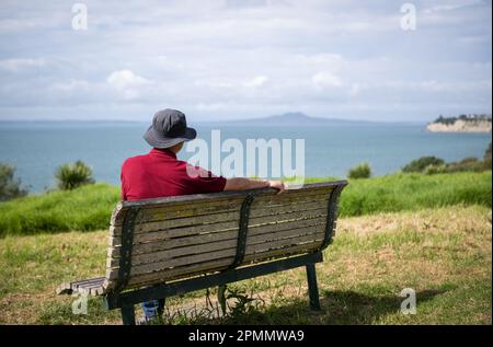 L'uomo gode delle viste mozzafiato del Golfo di Hauraki con l'Isola di Rangitoto in lontananza. Passeggiata costiera di Long Bay. Auckland. Foto Stock