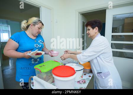 Infermiere in camici da laboratorio che forniscono ai pazienti piatti con cibo da un carrello a vassoio vicino alle stanze dei pazienti di un ospedale. Giugno 4, 2019. CityCenter di neurosurger Foto Stock