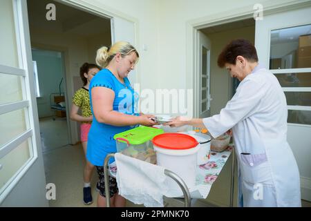 Infermiere in camici da laboratorio che forniscono ai pazienti piatti con cibo da un carrello a vassoio vicino alle stanze dei pazienti di un ospedale. Giugno 4, 2019. CityCenter di neurosurger Foto Stock