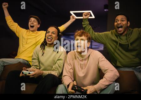 KIEV, UCRAINA - 13 FEBBRAIO 2023: Entusiasti giocatori interrazziali che giocano a videogame vicino amici in cyber club, immagine stock Foto Stock