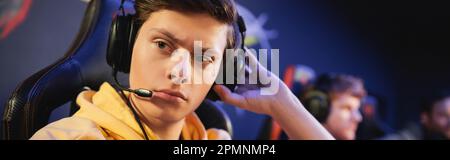 Videogamer concentrato in cuffie con microfono che guarda lontano in cyber club, banner, immagine stock Foto Stock