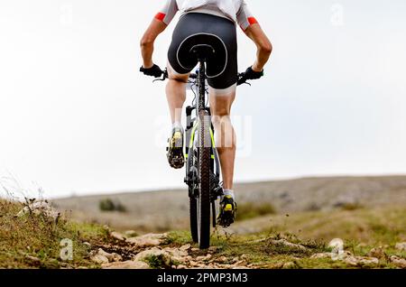 vista posteriore alpinista maschile in bicicletta su pista montagnosa in gara di sci di fondo Foto Stock