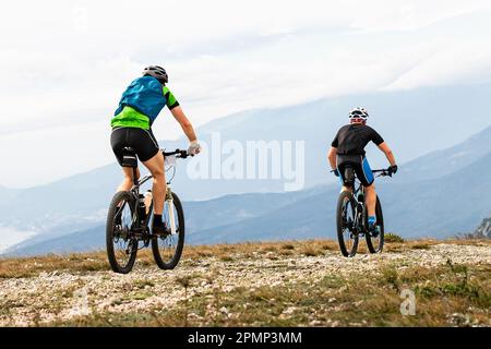 due alpinisti maschi che pedalano insieme pedalano su terreni montagnosi in bicicletta Foto Stock