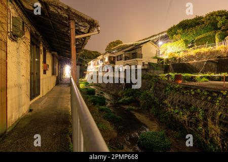 Passerella dal fiume scuro e vecchie case nella piccola città giapponese di notte Foto Stock