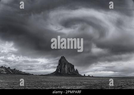 Nuvole che sembrano un vortice sopra Shiprock nella pianura desertica della Nazione Navajo nel New Mexico, USA, lavorate in bianco e nero Foto Stock