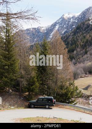 Auto parcheggiata su un tornante con montagne innevate e foreste alle spalle, vicino al villaggio di Lignan in Valle d'Aosta Foto Stock