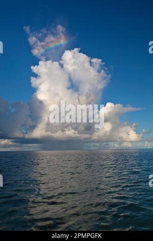 Un piccolo arcobaleno brilla sulle nuvole di tempesta sopra l'oceano; Seychelles Foto Stock