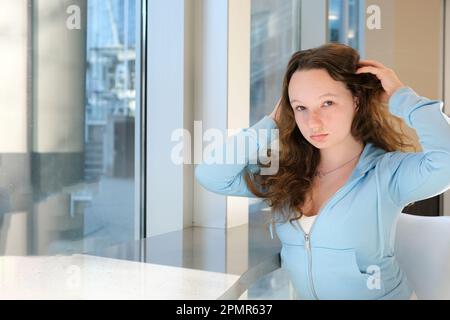 Bella ragazza alla tabella in ufficio raddrizza i capelli scuola privata di studio per essere bello eccellente studente perfetta bellezza tenera dell'adolescenza bianco faccia blu vestiti capelli puffy europeo ucraino Foto Stock