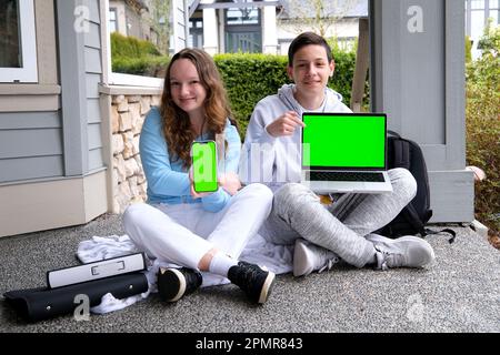 ragazzo teen e ragazza adolescente seduti all'aperto con cartelle zaino tenere laptop e telefono verde schermo chroma chiave annuncio guardare qui scuola presentazione sul computer. il bambino è pronto per una lezione video Foto Stock