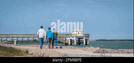PORT ARANSAS, TX - 10 FEB 2023: Tre persone camminano sul marciapiede del South Jetty verso il molo UT in una giornata di sole. Foto Stock