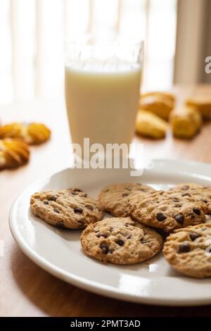 bicchiere di latte accanto a un piatto con biscotti al cioccolato, bevande deliziose e cibi fatti in casa, snack appetitosi Foto Stock