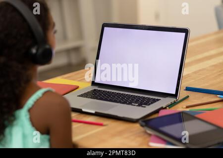 Ragazza biraciale focalizzata che indossa le cuffie e impara a casa utilizzando il laptop, copia spazio sullo schermo Foto Stock