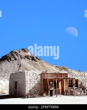 Vecchio stile occidentale adobe edificio luna e sfondo di montagna Foto Stock