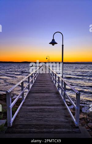 Lungo molo di legno al largo della spiaggia cittadina di Murrays Beach sul Lago Macquarie in Australia - scappatoia panoramica. Foto Stock