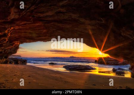 Sole che sorge sull'orizzonte dell'oceano Pacifico dall'interno della grotta di pietra arenaria della spiaggia di Caves. Foto Stock