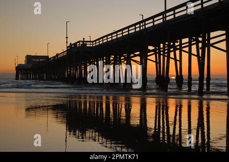 Il sole tramonta sull'Oceano Pacifico e sul molo di Newport, riflettendosi nelle acque della costa californiana Foto Stock