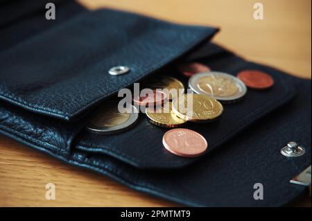 Monete in euro in portafoglio nero su tavolo di legno Foto Stock