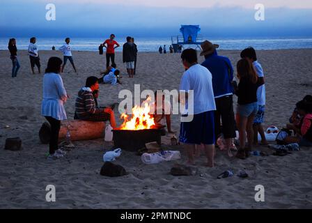 Amici e familiari si riuniscono intorno a un falò sulla spiaggia di Santa Cruz California per arrostire marshmallows e hot dog sopra il fuoco Foto Stock