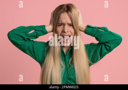 Non vuoi ascoltare e ascoltare. Frustrata irritata donna caucasica che copre le orecchie gesturing No, evitando consiglio ignorando sgradevole rumore voci forte. Bella ragazza da sola su sfondo rosa Foto Stock