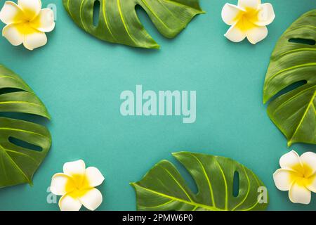 Sfondo estivo con fiori di frangipani tropicali e verdi foglie di palma tropicali su sfondo verde. Piano di giacitura, vista dall'alto. Festa in estate Foto Stock