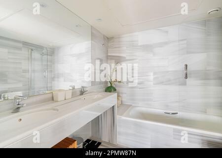 Bagno elegante con lavandino a specchio e armadietti sullo sfondo di una vasca in un nuovo appartamento. Il concetto di ristrutturazione di design in colori laconici Foto Stock