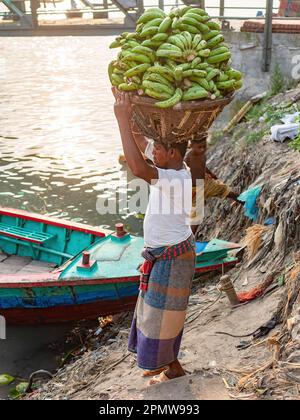 Uomo che trasporta mazzi di banane verdi ai traghetti locali alla stazione di nave di Wise Ghat sul fiume Buriganga a Dhaka, la capitale del Bangladesh. Foto Stock