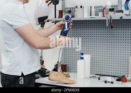 Ritagliare un artigiano irriconoscibile che regola e piega la gamba protesica moderna nella sezione del ginocchio Foto Stock