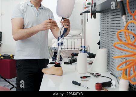 Ritagliare un artigiano irriconoscibile che regola e piega la gamba protesica moderna nella sezione del ginocchio Foto Stock