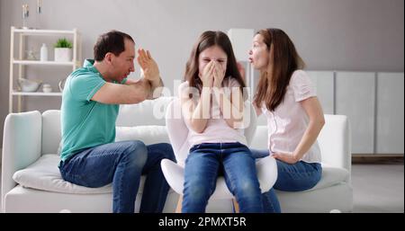 Genitore seduto sul divano Quarreling rumorosamente dietro la ragazza che copre le sue orecchie Foto Stock