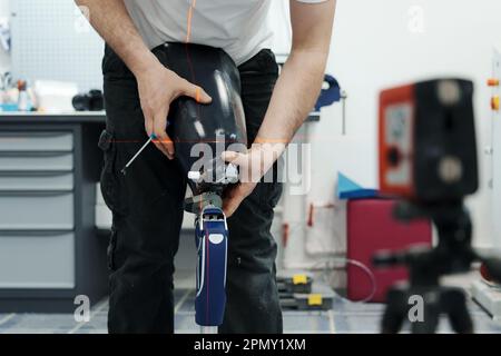 Ritagliare un artigiano irriconoscibile che regola e piega la gamba protesica moderna nella sezione del ginocchio Foto Stock