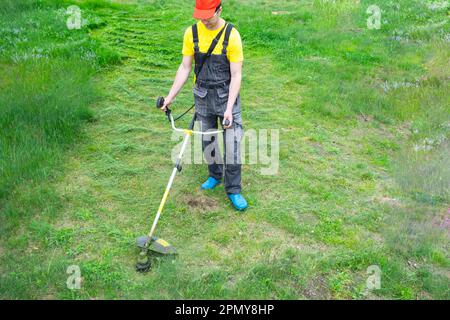 Un giardiniere maschio taglia l'erba verde del prato nel cortile